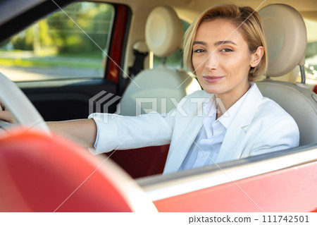 Woman wearing official style suit keeping steering wheel in car 111742501