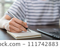 Close-up of hand writing on blank notebook on table. 111742883