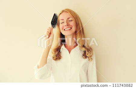 Portrait of happy smiling caucasian blonde young woman combing her hair with comb 111743082