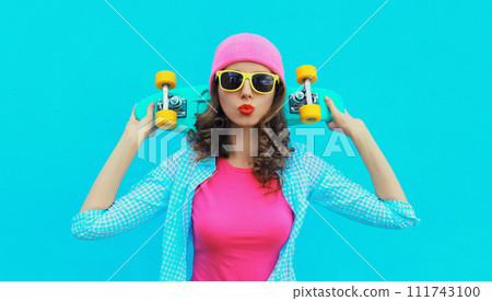 Portrait of stylish modern young woman with skateboard posing in colorful vivid clothes, pink hat 111743100