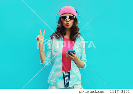 Portrait of stylish modern happy young woman listening to music in headphones with mobile phone 111743101