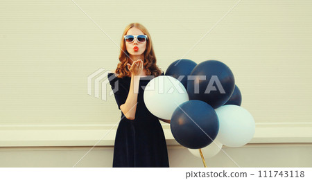 Beautiful happy young woman with bunch of black and white balloons in summer dress blowing kiss Beautiful happy young woman with bunch of black and white balloons in summer dress blowing kiss 111743118