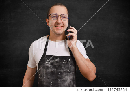 Portrait of a happy male chef with a phone in his hands, looking at the camera on a dark background Portrait of a happy male chef with a phone in his hands, looking at the camera on a dark background 111743834