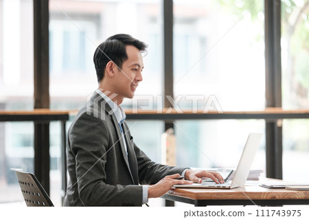 Young Businessman Using Laptop Computer in Modern Office. Manager Thinks About Successful Financial Ideas. Happy Man Smiling About Finding Problem Solving Solutions for Company. Young Businessman Using Laptop Computer in Modern Office. Manager Thinks About Successful Financial Ideas. Happy Man Smiling About Finding Problem Solving Solutions for Company. 111743975