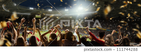 Sport match event. Back view of football fans cheering favorite soccer team at crowded stadium at evening time. Winning championship 111744288