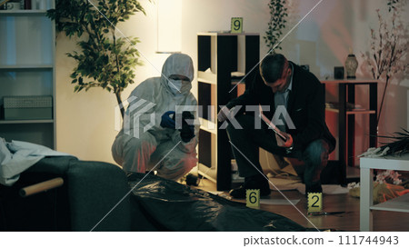 A police detective and a forensic analyst are examining the murder scene and gathering evidence A police detective and a forensic analyst are examining the murder scene and gathering evidence 111744943