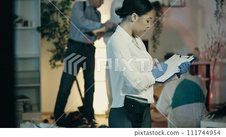 A female police detective is filling out evidence preservation documents at the crime scene 111744954