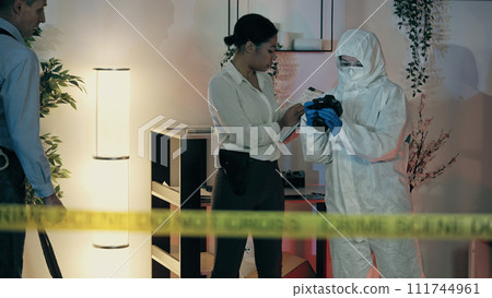A woman detective is looking through evidence photos and making notes about the crime scene 111744961