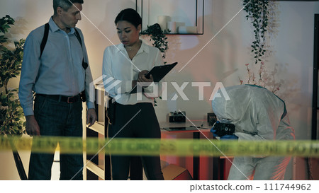 Two detectives are discussing the crime scene while a forensic expert takes pictures of the evidence Two detectives are discussing the crime scene while a forensic expert takes pictures of the evidence 111744962