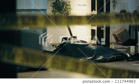 A dead body is lying on the floor in a plastic bag, with evidence markers in a messy room, signifying a murder scene 111744963