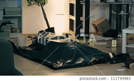 The body of a dead person is lying on the floor, covered with a plastic corpse bag at the trashed crime scene with evidence markers The body of a dead person is lying on the floor, covered with a plastic corpse bag at the trashed crime scene with evidence markers 111744965