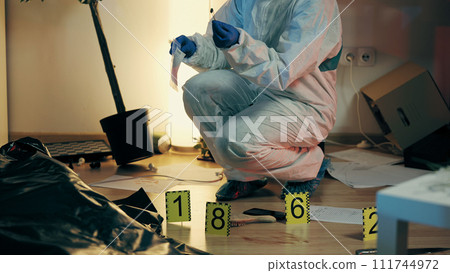 A forensic police expert is collecting a bullet case in an evidence bag and examining the murder scene A forensic police expert is collecting a bullet case in an evidence bag and examining the murder scene 111744972