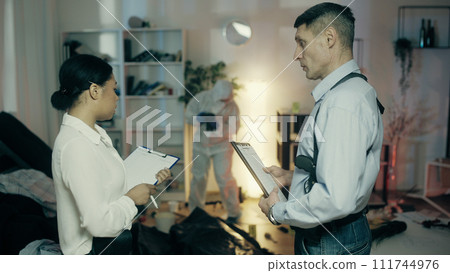 An African American detective and her colleague are documenting and discussing evidence at the crime scene An African American detective and her colleague are documenting and discussing evidence at the crime scene 111744976
