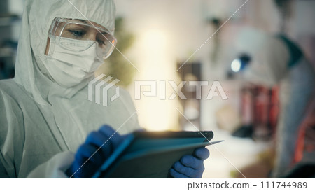 A forensic expert with a tablet is analyzing photos of the crime scene as part of the investigation 111744989