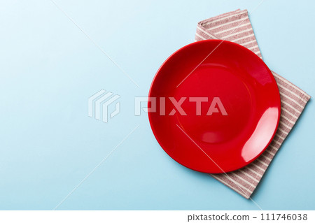 Top view on colored background empty round red plate on tablecloth for food. Empty dish on napkin with space for your design Top view on colored background empty round red plate on tablecloth for food. Empty dish on napkin with space for your design 111746038