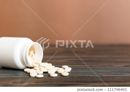Medicine bottle and white pills spilled on a light background. Medicines and prescription pills flat lay background. White medical pills and tablets spilling out of a drug bottle 111746401