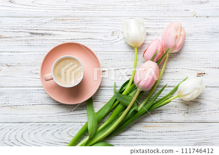 Spring background with flowers, a cup of coffee and a bouquet of pink and white tulips on colored table background with place for text. Copy space top view 111746412
