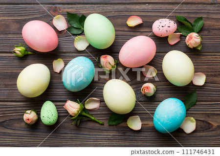 Happy Easter. Easter eggs on colored table with yellow roses. Natural dyed colorful eggs background top view with copy space Happy Easter. Easter eggs on colored table with yellow roses. Natural dyed colorful eggs background top view with copy space 111746431
