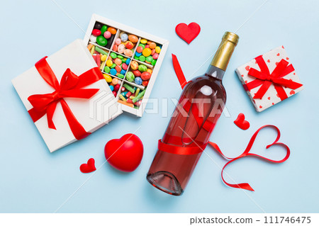 Bottle of red wine on colored background for Valentine Day with gift and chocolate. Heart shaped with gift box of chocolates top view with copy space 111746475