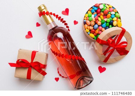 Bottle of red wine on colored background for Valentine Day with gift and chocolate. Heart shaped with gift box of chocolates top view with copy space 111746480
