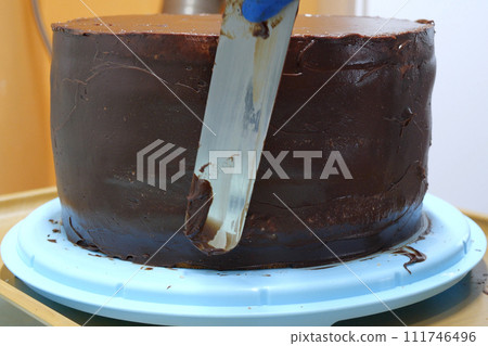 Confectioner woman is smearing cream on sides of cake using spatula, closeup view. culinary, baking and cooking food concept, home cooking Confectioner woman is smearing cream on sides of cake using spatula, closeup view. culinary, baking and cooking food concept, home cooking 111746496