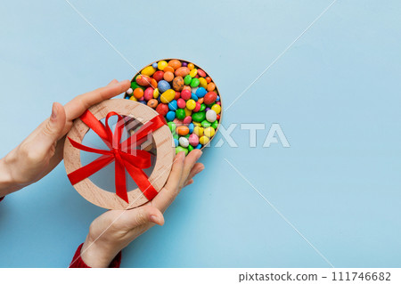 Female hands with delicious candies in box on color background 111746682