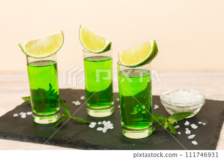 Sweet refreshing mint liqueur, with ice and mint leaves on table background, Shots with lime slice and mint flat lay 111746931