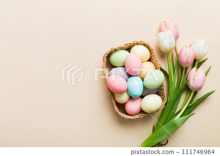 Happy Easter composition. Easter eggs in basket on colored table with yellow Tulips. Natural dyed colorful eggs background top view with copy space Happy Easter composition. Easter eggs in basket on colored table with yellow Tulips. Natural dyed colorful eggs background top view with copy space 111746964