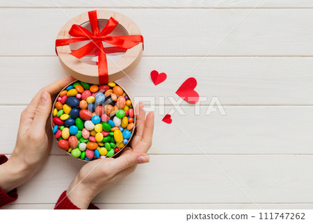 Female hands with delicious candies in box on color background 111747262