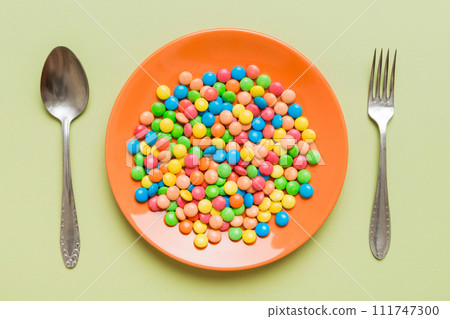 cutlery on table and sweet plate of candy. Health and obesity concept, top view on colored background cutlery on table and sweet plate of candy. Health and obesity concept, top view on colored background 111747300