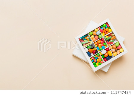 Set of different sweet candy in a paper box with a satin ribbon on a colored background. Holiday concept Set of different sweet candy in a paper box with a satin ribbon on a colored background. Holiday concept 111747484