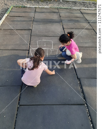 Two little girls drawing by charcoal in ground Two little girls drawing by charcoal in ground 111747671