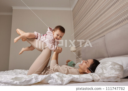 Happy Caucasian mother raising laughing cute baby and playing together in bedroom 111747782