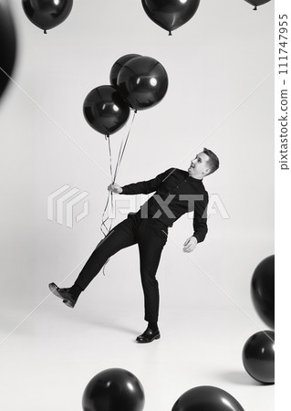 elegant caucasian man with bunch of black air balloons on white background. black and white elegant caucasian man with bunch of black air balloons on white background. black and white 111747955