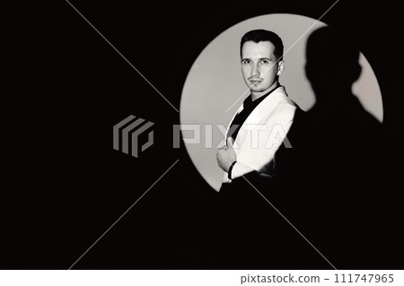 elegant man in white suit tuxedo in the circle of light, copy space. black and white elegant man in white suit tuxedo in the circle of light, copy space. black and white 111747965