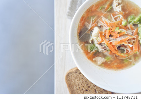 Top view of a healthy and delicious soup of vegetables and meat in a white plate on the table with bread with copy space on the left. Homemade soup for restaurant menus, cafes, food delivery. Top view of a healthy and delicious soup of vegetables and meat in a white plate on the table with bread with copy space on the left. Homemade soup for restaurant menus, cafes, food delivery. 111748711