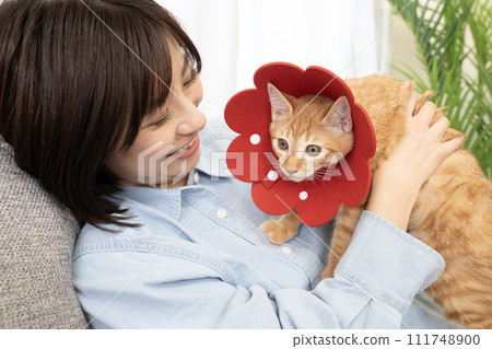 A smiling woman with a kitten with a red Elizabethan collar 111748900