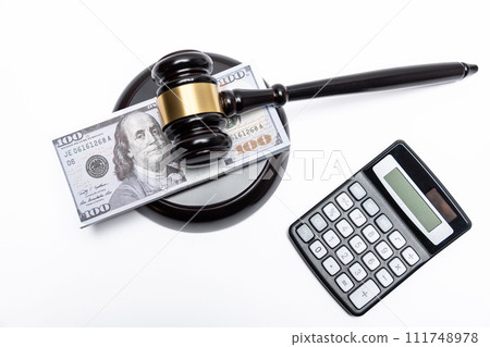 A legal gavel atop American currency with a calculator, depicting financial law or fines. A legal gavel atop American currency with a calculator, depicting financial law or fines. 111748978