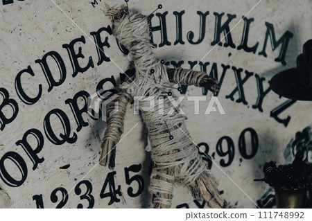 A dark atmospheric setting with an Ouija board, candles, and mystical objects invoking a sense of the occult. A dark atmospheric setting with an Ouija board, candles, and mystical objects invoking a sense of the occult. 111748992