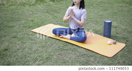 A woman wearing yoga wear sits and meditates in a park A woman wearing yoga wear sits and meditates in a park 111749053