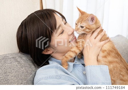 A woman kisses a kitten on the nose on the sofa 111749184