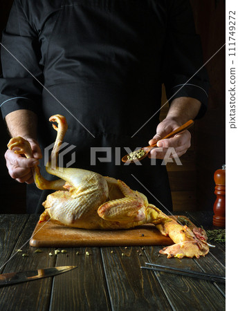 A chef prepares raw chicken in the kitchen of a public house. Before frying, the cook adds spices to the broiler 111749272