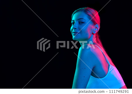 portrait of positive young woman looking at camera against black studio background in colorful neon light. Negative space to insert text. portrait of positive young woman looking at camera against black studio background in colorful neon light. Negative space to insert text. 111749291