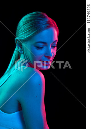 Tender, half-naked woman posing in underwear against black studio background in colorful neon light. Tender, half-naked woman posing in underwear against black studio background in colorful neon light. 111749298