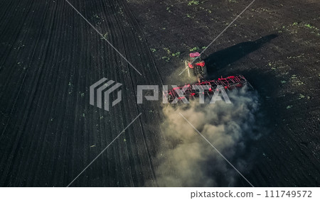 Aerial view of red tractor plows the ground 111749572