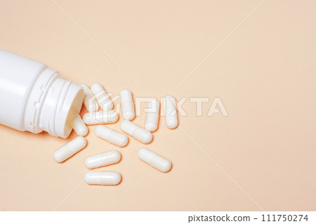 White pills spilling out of pill bottle on beige background with copy space . White pills medicine 111750274