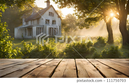 An empty wooden table in the foreground, with a blurred country house in the background against a verdant garden setting 111750703
