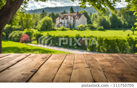 An empty wooden table in the foreground, with a blurred country house in the background against a verdant garden setting An empty wooden table in the foreground, with a blurred country house in the background against a verdant garden setting 111750709
