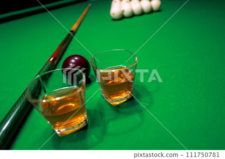 Glass of whiskey on billiard table with cue and billiard balls in background Glass of whiskey on billiard table with cue and billiard balls in background 111750781