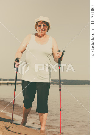 Senior woman practicing nordic walking on beach 111751005